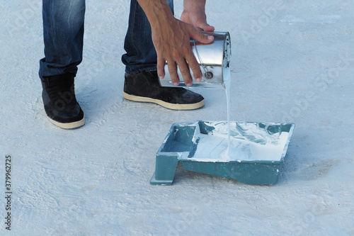 Man pouring white waterproof paint from bucket in container at roof.