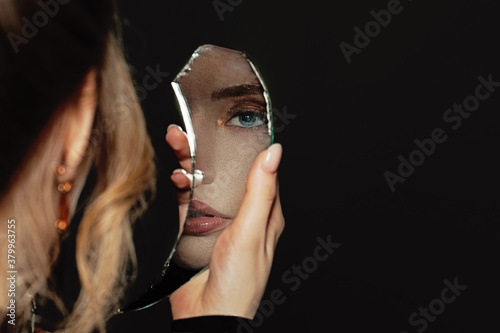 Fotografie Young perfect woman holding broken self-image mirror on black background