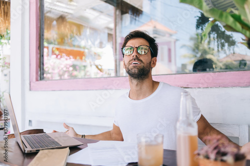 Happy young male freelancer sitting at table in outdoor cafe in summer