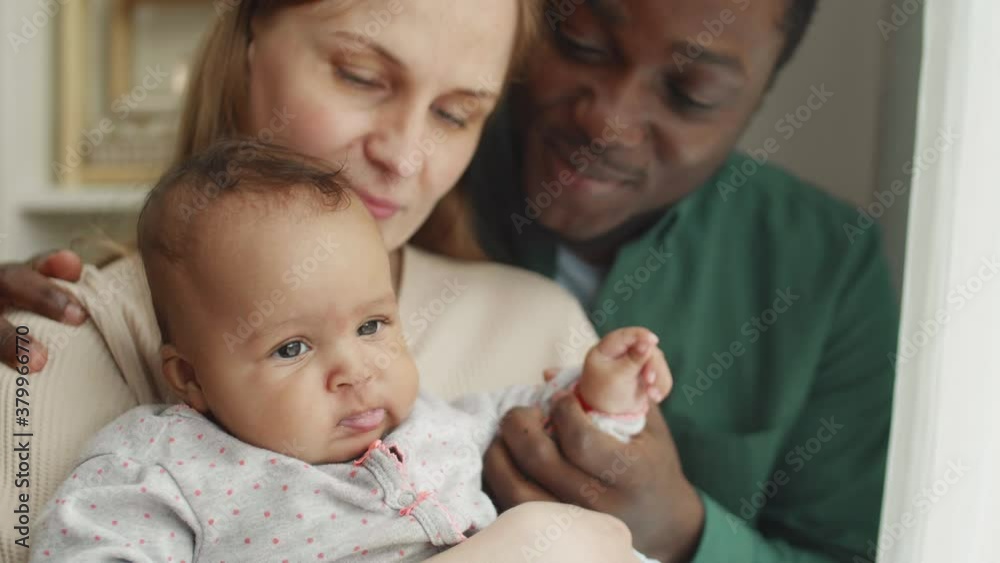 Close up of Caucasian woman holding mixed-race baby in her hands while her handsome husband standing behind her, hugging her and holding small palm of the kid Close up of Caucasian woman holding mixed-race baby in her hands while her handsome husband standing behind her, hugging her and holding small palm of the kid