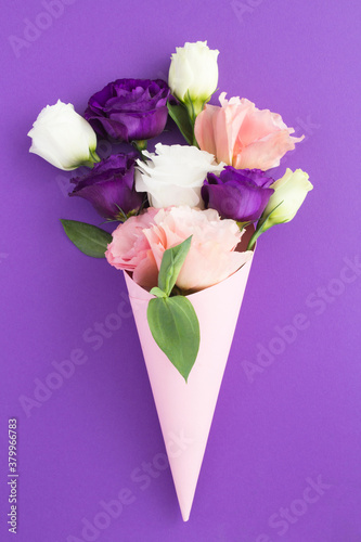 White, pink and violet flowers in a paper pink cone on the violet background. Location vertical.