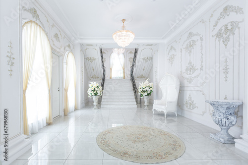 luxury royal posh interior in baroque style. very bright, light and white hall with expensive oldstyle furniture. chic wide marble staircase leading to the second floor photo