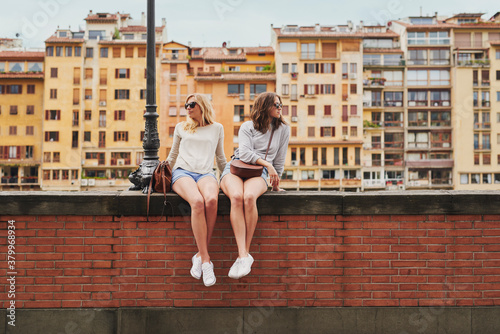 Two tourist girl friends relaxing on historical bridge in Floren