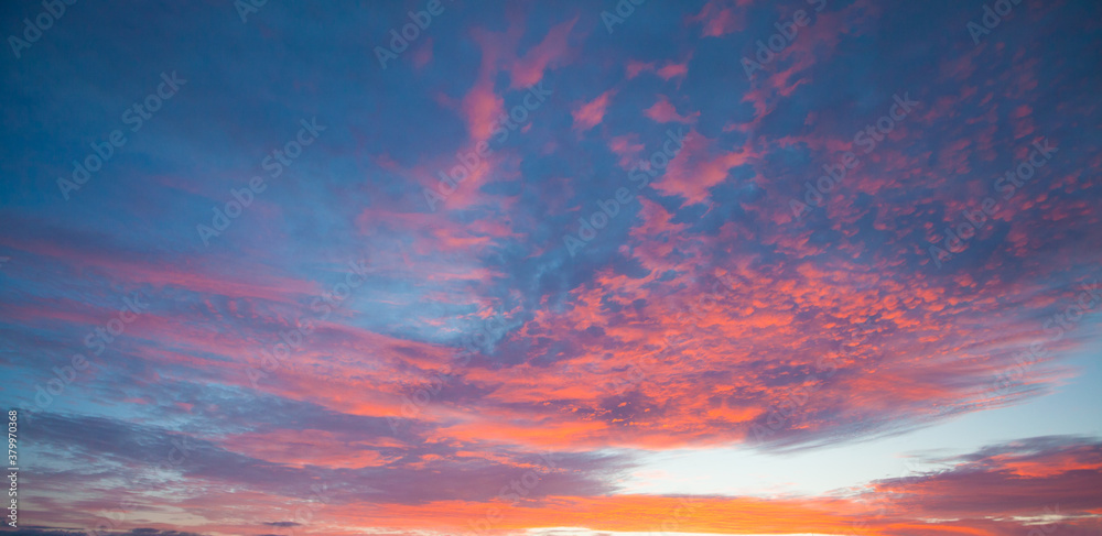 Red and blue sunset sky with clouds and sun