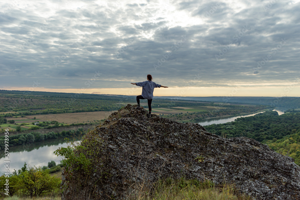 Girl on top of a cliff over the Dniester river in summer at sunset.