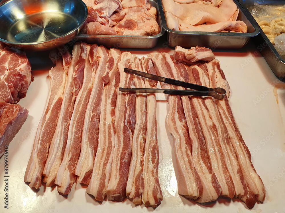 Organic pork belly cut into long strips on a fresh pork stall and there are tongs next to it. Pork belly contains the nutrients, proteins and fats needed to repair the wear and tear of the body.
