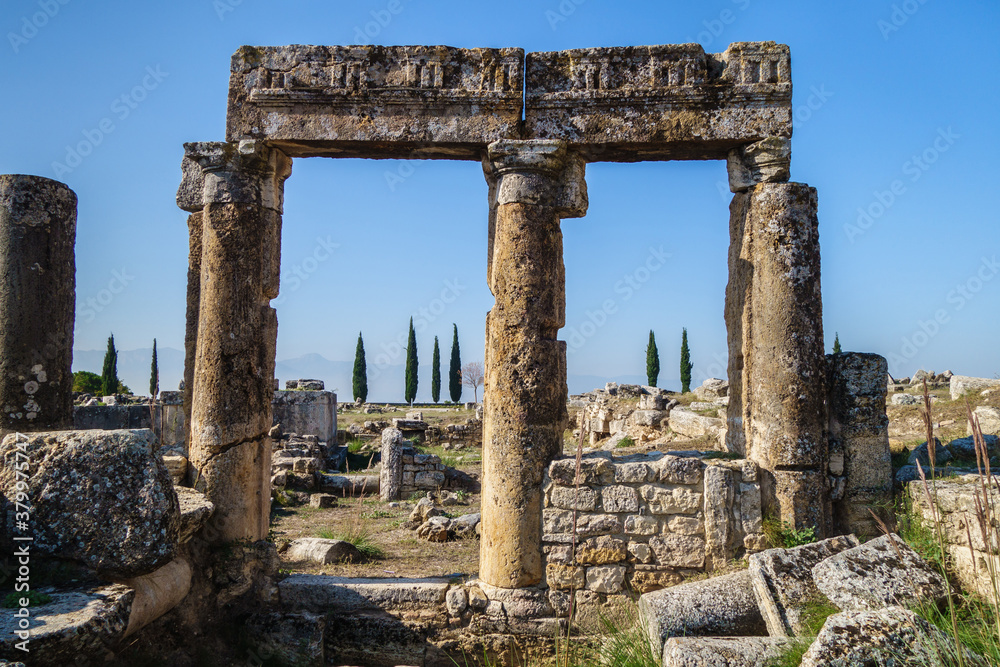 Close view on ancient columns & its elements in antique city Hierapolis, Pamukkale, Turkey. Located near former colonnaded Frontinus street. Ruins of buildings on background. City included in UNESCO