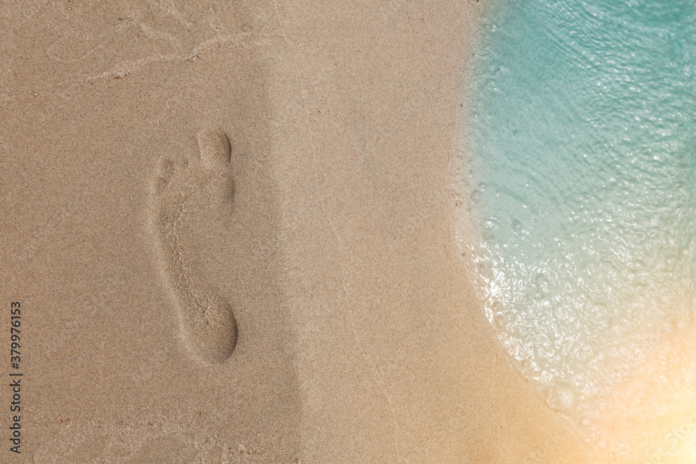 Footprint of a man on a sandy beach top view next to the coastline and turquoise sea water. Background for banner or tourist brochure or advertisement.