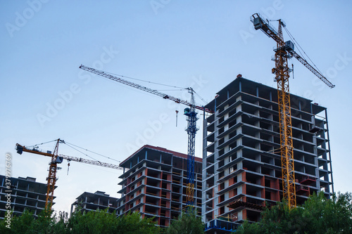 Several high-rise buildings under construction and cranes next to them photo