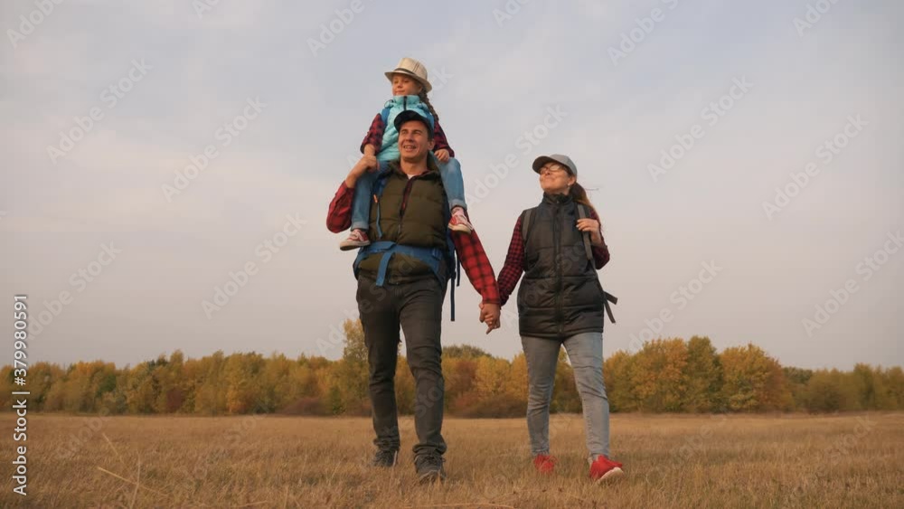 Happy friendly family is walking on a picnic. The father carries his daughter on his shoulders. The child is enjoying family fun. Lifestyle concept, family hiking. The kid walks with dad and mom. Happy friendly family is walking on a picnic. The father carries his daughter on his shoulders. The child is enjoying family fun. Lifestyle concept, family hiking. The kid walks with dad and mom.