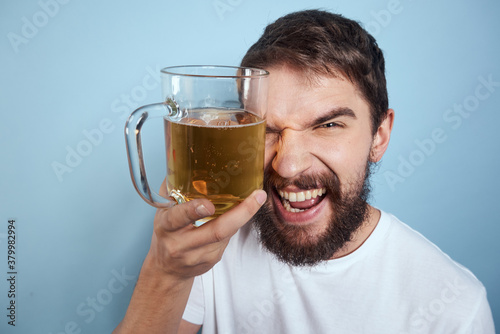 Cheerful man in a white T-shirt with a beer mug drunk blue background