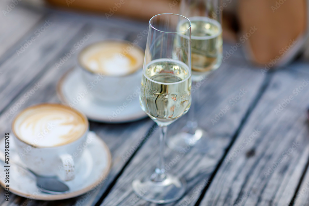 Obraz premium Closeup of two glasses of champagne and two cups of cappuccino or coffee for romantic breakfast in outdoor cafe or hotel restaurant