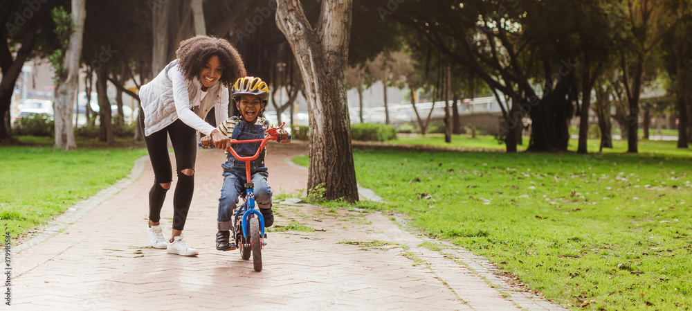 Little boy learning to ride bicycle at park with mother - obrazy, fototapety, plakaty 