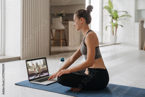 Yoga teacher conducting virtual yoga class at home on a video conference. Beautiful fit woman practicing online yoga in her living room with laptop. Home fitness and workout concept. Online training