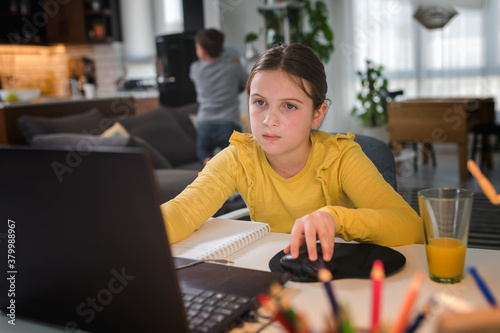 Preteen schoolgirl doing her homework with laptop computer at home. Child using gadgets to study. Online education and distance learning for kids. Homeschooling during quarantine
