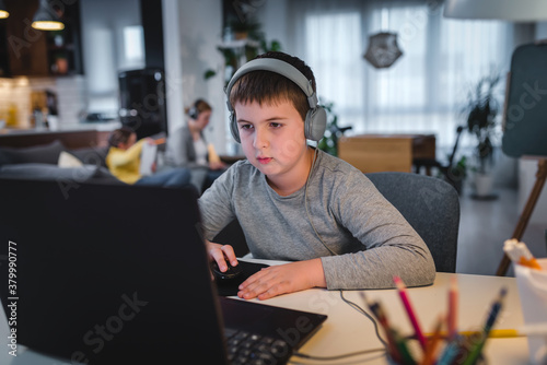 Cute boy with headphones using laptop computer for online learning. Home school. Child doing homework at home. Lifestyle concept for home schooling. Social distancing and education.