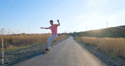 Young male ride on longboard skateboard on the country road in sunny day 