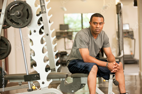 African American man resting in health club on weight-lifting bench photo