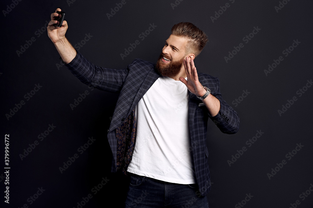 Handsome bearded businessman in suit making selfie isolated on black