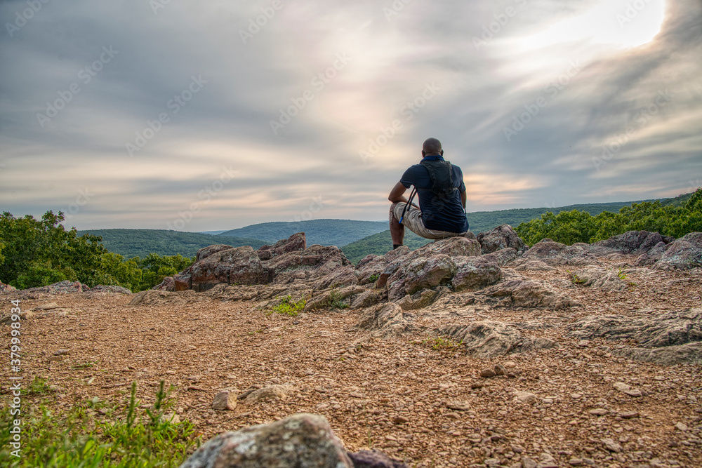 African American man sitting at the the top of a mountain enjoying the view during a hike.