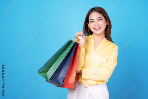 Happy beautiful Asian woman carrying colorful shopping bags, Isolated on a blue background.