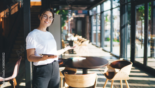 Positive young hostess inviting guests to cafe photo