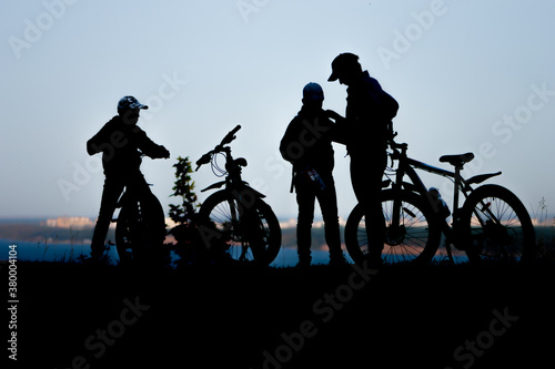 Silhouettes of figures of a father with two sons on a Bicycle ride in the Park by the river. The concept of a healthy lifestyle in the family.