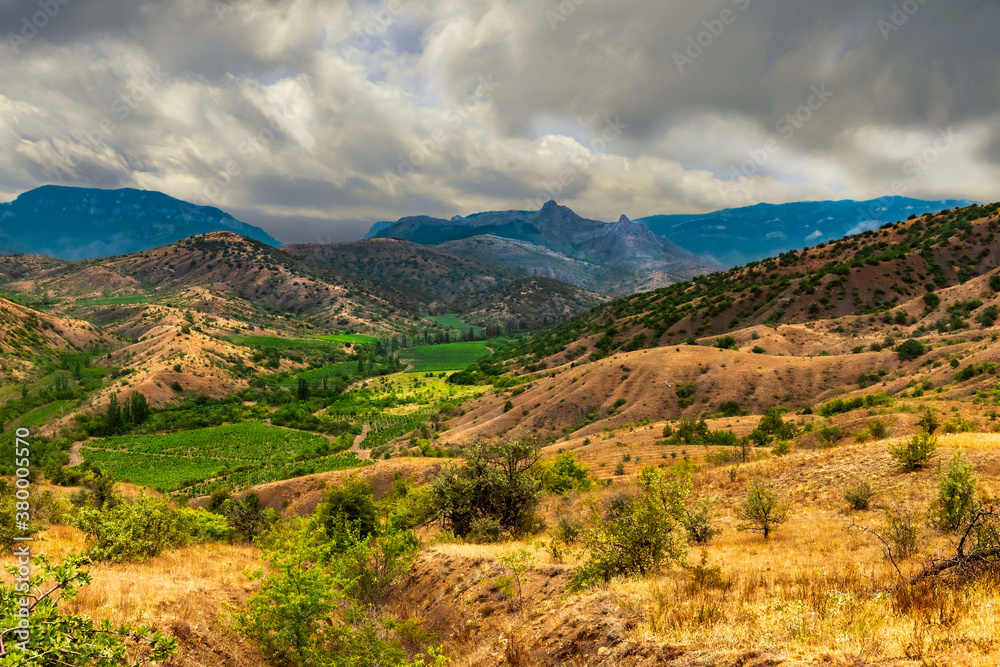 Landscape of the Crimean mountains, covered by approaching storm clouds, and a valley with vineyards