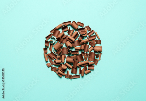 Chocolate pieces in a circle on a blue background. Chocolate curls top view
