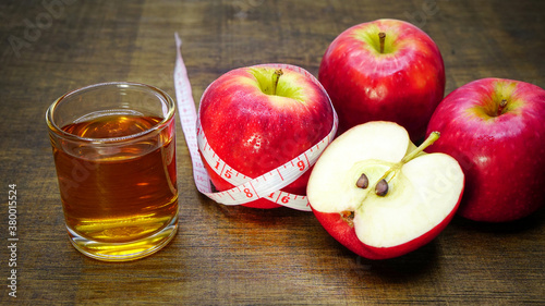 Apple cider vinegar in a glass with apples and a measuring tape on a wooden background.