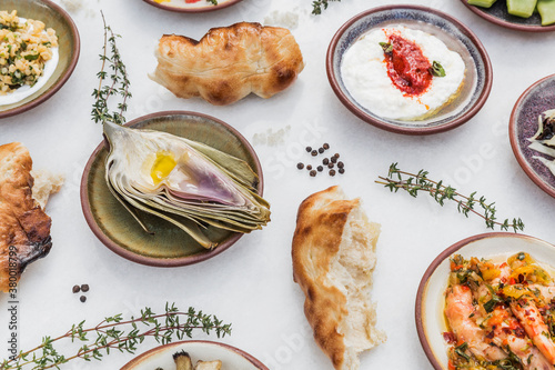 Roasted artichoke surrounded by small dishes and bread photo