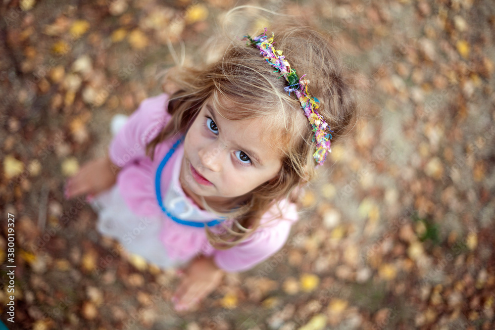 Young girl in pink princess dress with colorful headband looks upward Young girl in pink princess dress with colorful headband looks upward