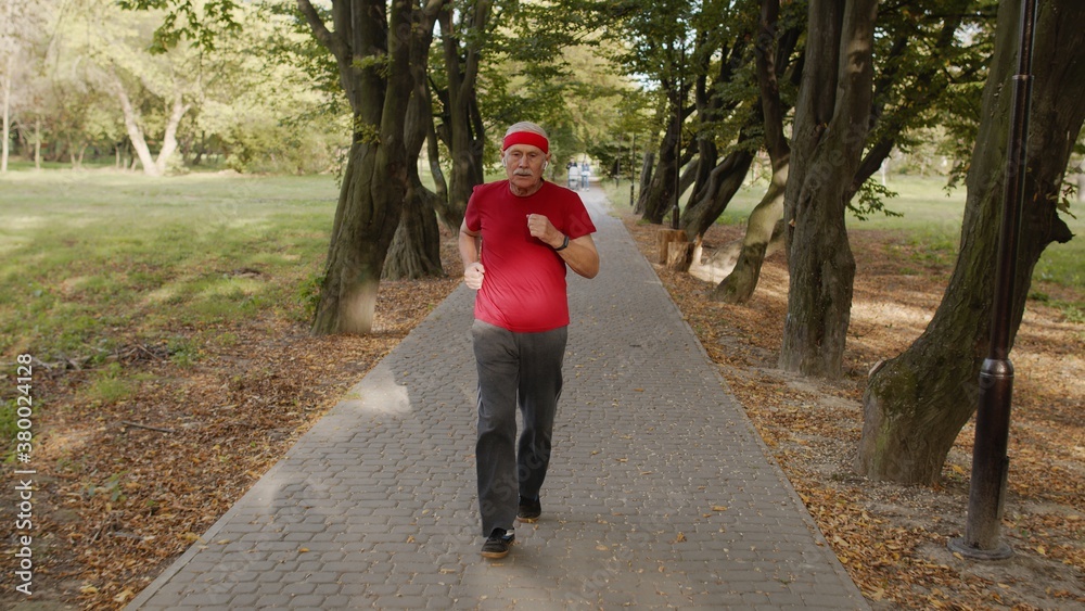 Senior old man running, working out cardio in park and using bluetooth earphones, listening music Senior old man running, working out cardio in park and using bluetooth earphones, listening music