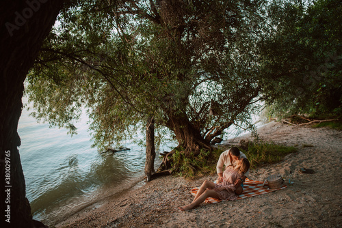 An attractive blonde caucasian woman lies in the arms of a man on the beach. A loving couple on a picnic by the river