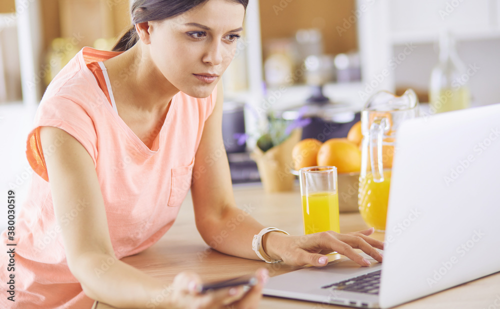Pretty woman on the phone using laptop at home in the kitchen Pretty woman on the phone using laptop at home in the kitchen