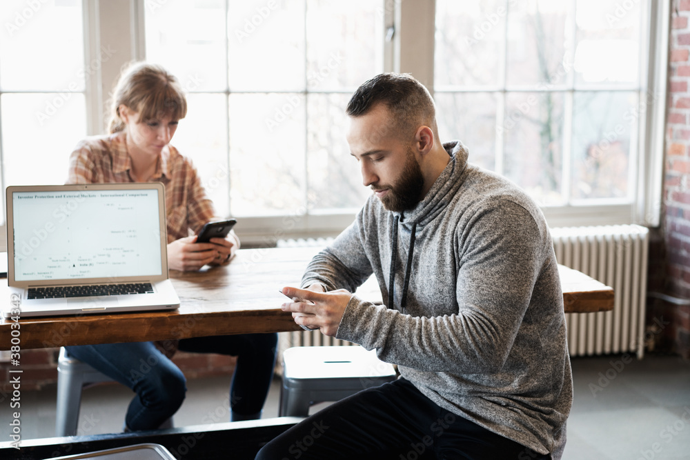 Man and woman at office table look down at their own cell phones Man and woman at office table look down at their own cell phones