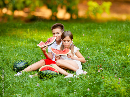 boy and girl sit on the grass and eat watermelon © Julie Boro