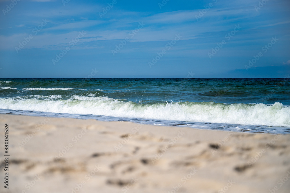 Stormy surf on the seashore, with white foam on the yellow sand. Skyline over the sea with blue sky and cumulus clouds Stormy surf on the seashore, with white foam on the yellow sand. Skyline over the sea with blue sky and cumulus clouds
