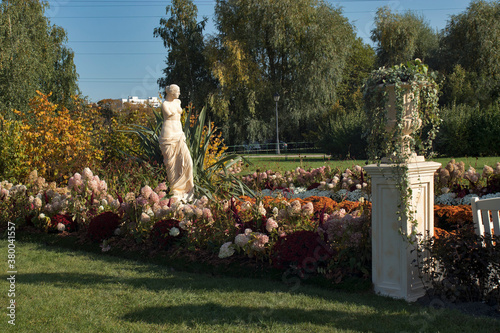 The plaster statue of Venus is reflected in small pond lined with yellow and red chrysanthemums and hydrangeas. photo