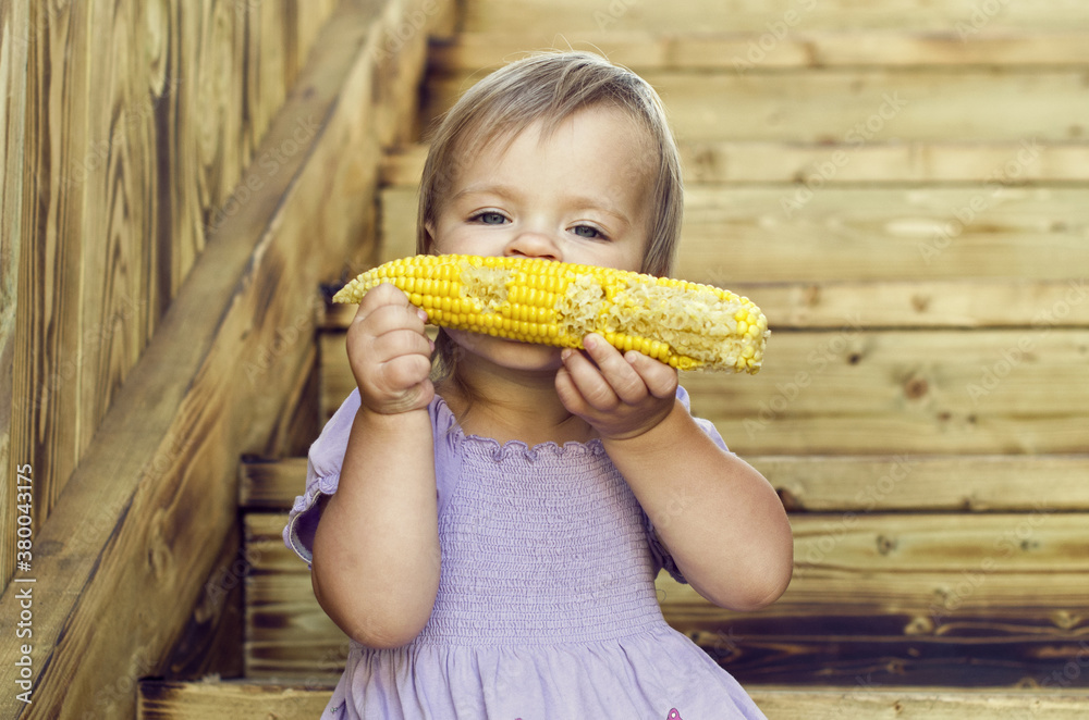 Little blonde girl eating corn of wooden background Little blonde girl eating corn of wooden background