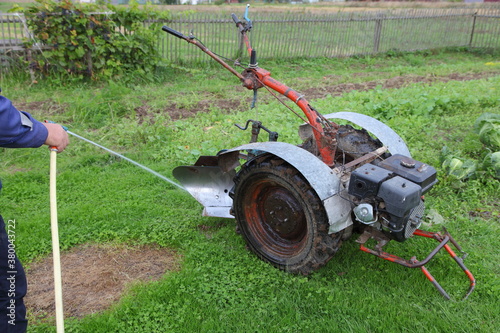 Old Motor cultivator with auxiliary plow washing with water stream on green grass background at summer day, mini tractor service, farming mechanization maintenance