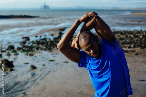 A man in a blue top stretching on an empty beach