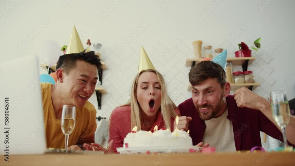 Attractive mixed-race adult friends celebrating party anniversary at home. Men and woman dancing into music blowing candles on birthday cake having fun. Communication.