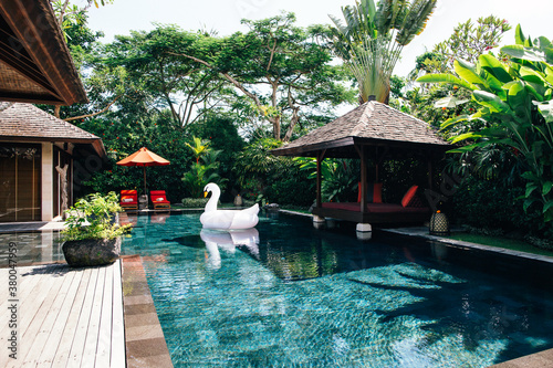 White Inflatable Toy Swan Floating in Pool of Luxurious Tropical Resort Villa photo