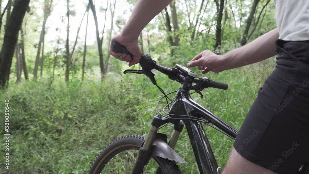 Man uses smart bicycle computer fixed on handlebars mountain bike, cyclist using navigator to find GPS coordinates while cycling in forest. Cycle computer with offline maps for tourism and travel. Man uses smart bicycle computer fixed on handlebars mountain bike, cyclist using navigator to find GPS coordinates while cycling in forest. Cycle computer with offline maps for tourism and travel.