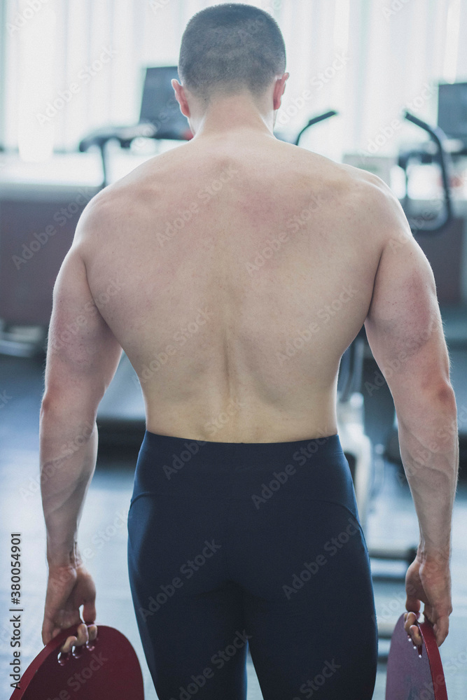 Fototapeta premium athlete with a wide muscular back goes with metal pancakes in the gym