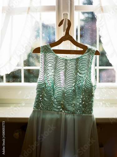 Sequin party dress hanging from window in sunlight