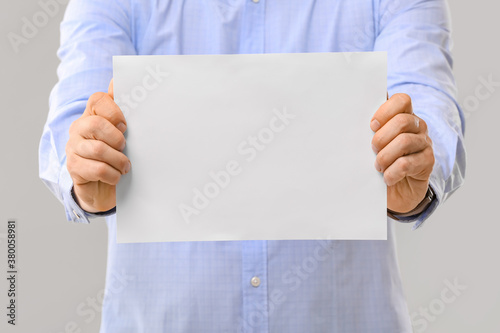 Man with blank paper sheet on grey background © Pixel-Shot