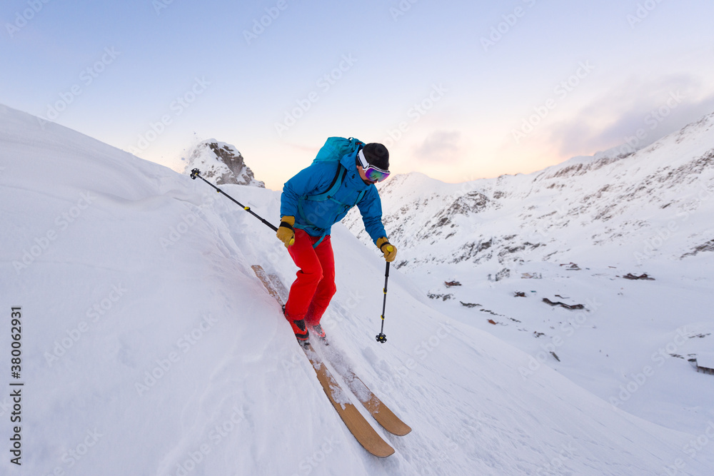 Man skiing downhill a steep slope during sunset Man skiing downhill a steep slope during sunset