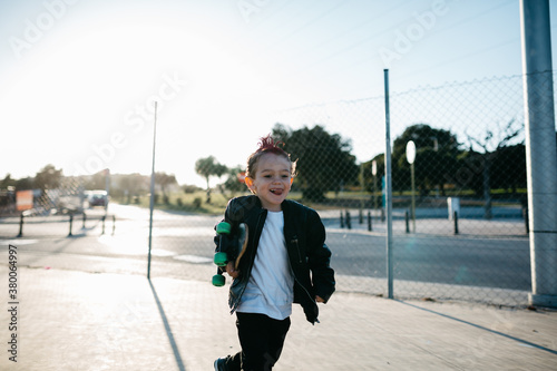 Cheerful kid with mohawk running with skateboard. photo